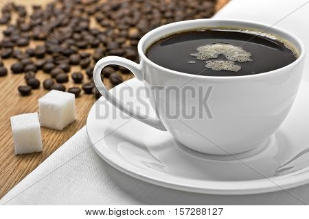 Coffee cup on a table, coffee beans and lump sugar around, studio shot