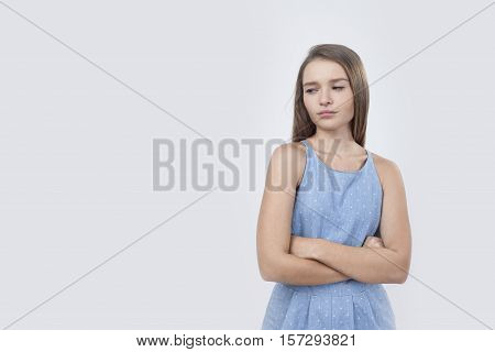 Portrait of offended European woman in blue dress who is standing against white background with her arms crossed and looking displeased. Mock up