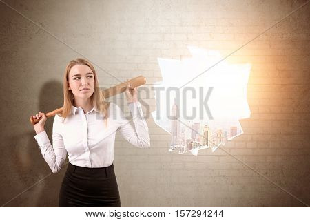 Businesswoman has crashed a white brick wall with sledgehammer. Sunlit New York City is seen through the hole. Concept of road to success. Toned image