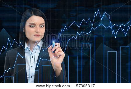 Close up of a businesswoman with black hair drawing graphs on glassboard. World map is seen in the background. Double exposure.
