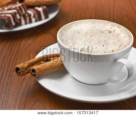 Cappuccino with cinnamon bark and plate of sweets on the table