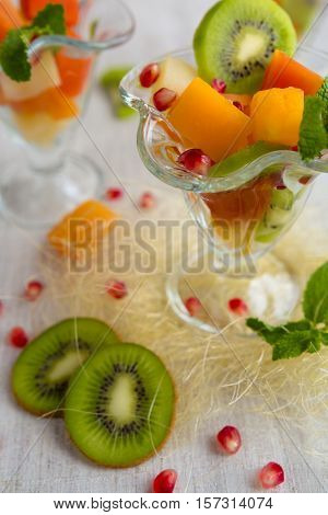 Fruit desserts, salad of pineapple, papaya, pomegranate and mint, kiwi on light background