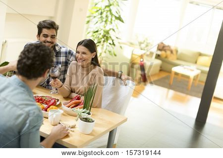 Group of happ young people sitting by the table eating and drinking red wine