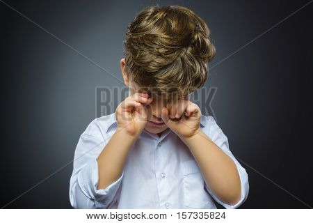Closeup Portrait of crying boy with astonished expression while standing against grey background.