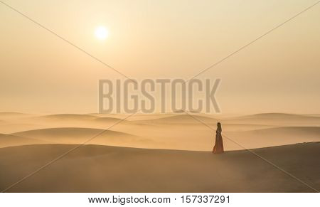 A woman in a mist in desert landscape at Sunraise near Dubai UAE