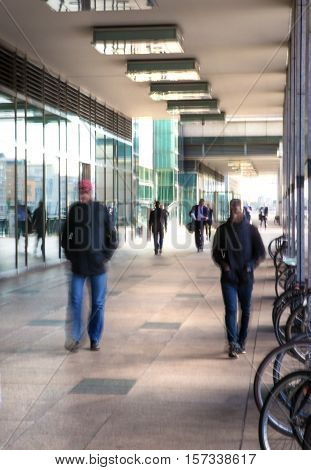 Abstract, blurred image of people walking via long tunnel with light at the background.
