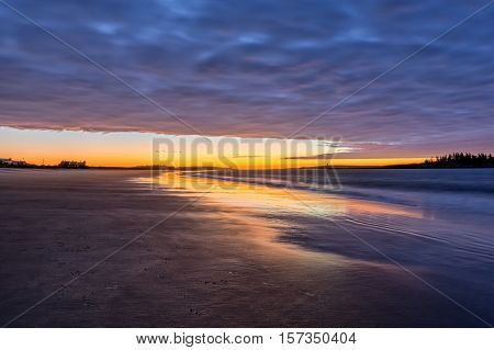 Sunrise at Popham State beach Maine. Smooth samd shore reflecting the cool golden sunlight