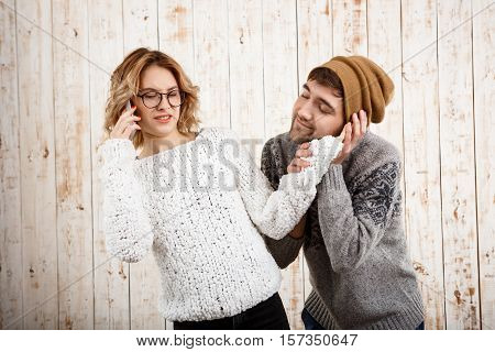 Young handsome man unnerve his girlfriend speaking on phone over wooden background. Copy space.