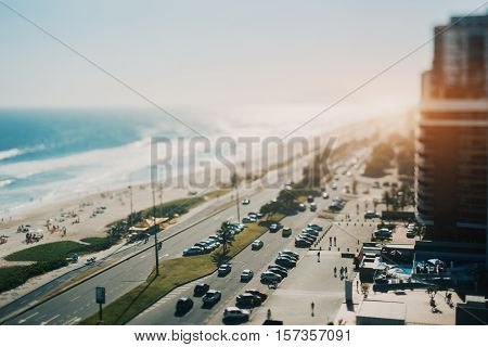 True tilt shift shooting of street with a lot of cars near ocean coastline with beach and many resting people summer sunny day Rio de Janeiro Brazil