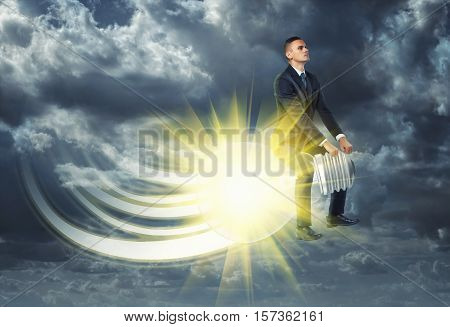 A businessman flying away on a lit light bulb on the overcast sky background. Business development and the way to success. The development of electricity and elektrotechniks. Improving the ability of enterprises. Prsonal growth and new ideas.