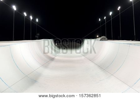 Snowboarder in a snow halfpipe night lit up by lights