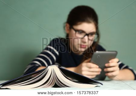 teenager lazy girl in myopia glasses play online game on tablet refuse to read book laughing entertain herself
