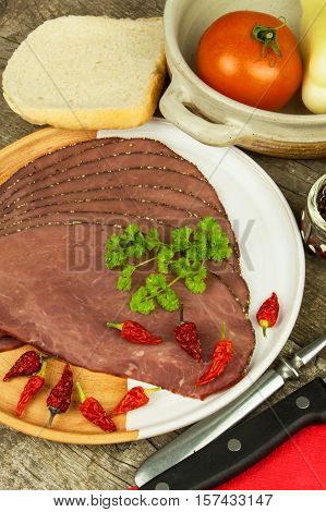 Cold roast beef on a wooden table. Delicacy of beef. Preparing cold refreshments. Traditional meal. Beef roast beef with green pepper and chili peppers and vegetables.