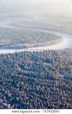 Aerial view of countryside road which is near forest river during cold winter day. Magnificent hoarfrost is on trees. A winter forest is in a hard frost.