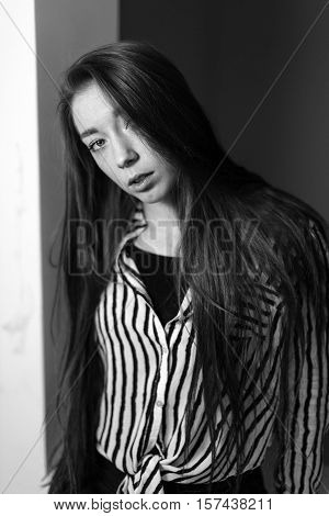 Portrait of a seated girl. Hair is covering half of her face. Portrait in black and white.