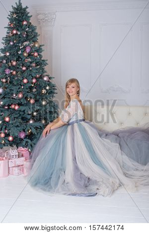 Blonde girl in evening dress sitting on a sofa in the new year eve