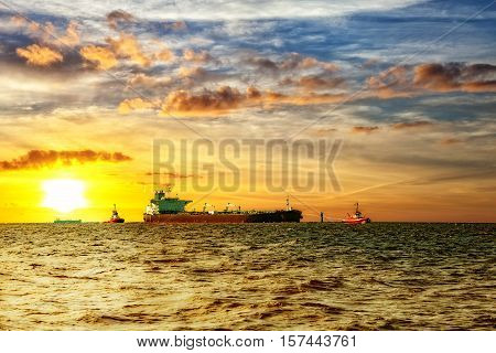 Tanker ship with escorting tugs on sea at sunrise.