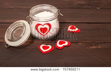 Jar with snow and a heart in him. A background from brown boards on boards several hearts are scattered the glass jar a heart from fabric lies in snow