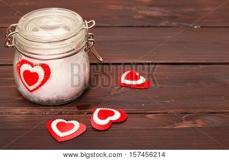 Jar with snow and a heart in him. A background from brown boards on boards several hearts are scattered the glass jar a heart from fabric lies in snow