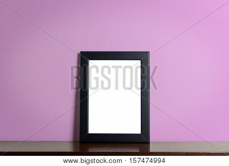 Blank photo frane on wooden shelf with pink background.