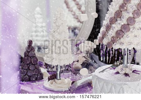 Beautiful set of three handmade white and purple croquembouche wedding cakes made from meringue and macarons standing on small dessert table reflecting in mirror