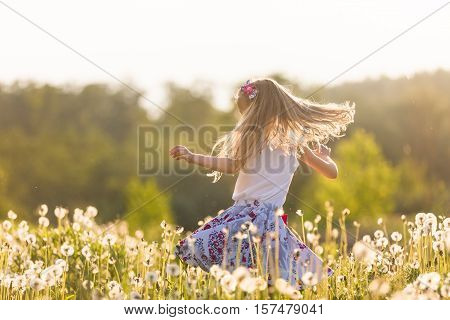 Girl running on the field of dandelions on summer sunset. Beautiful little kid girl dancing on dandelion meadow with summer sunset. Summer fun outdoors.