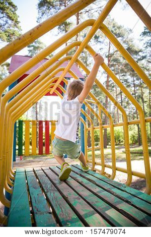 Portrait of cute kid boy playing on the climbing frame. Young boy climbing on playground during summer. Child enjoys climbing through a tunnel in a children's playground outdoors.