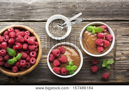 Chocolate Banana Smoothies served fresh juicy ripe raspberries with a sprig of mint in portioned bowls on a wooden background. The horizontal design