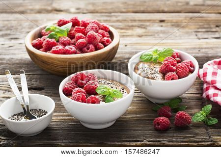 Chocolate Banana Smoothies served fresh juicy ripe raspberries with a sprig of mint in portioned bowls on a wooden background. The horizontal design