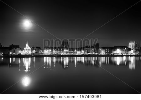 Supermoon rising over Kings Lynn harbour in Norfolk UK. Black and white landscape of building night lights and water reflection light up the harbour after dust