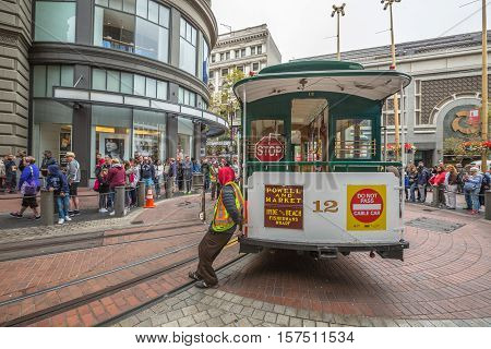 San Francisco, CA, USA - August 15, 2016: Cable car operators push the turntable around the reverse direction in Powell and Market St Turntable or terminus while crowds of tourists waiting to go up.