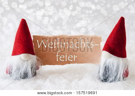German Text Weihnachtsfeier Means Christmas Party. Christmas Greeting Card With Two Red Gnomes. Sparkling Bokeh Background With Snow. English Text Seasons Greetings