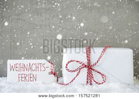 One Christmas Present On Snow. Cement Wall As Background With Snowflakes. Modern And Urban Style. Card For Birthday Or Seasons Greetings. Label With German Text Weihnachtsferien Means Christmas Break