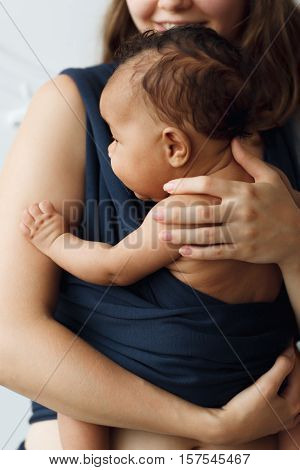 Mother holding her baby in sling. Newborn child hugs his mom in dark blue carrier, close-up. Happy family, care, modern motherhood concept