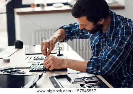Laptop disassembling with screwdriver, side view. Engineer fixing broken computer motherboard. Electronic repair shop, technology development concept