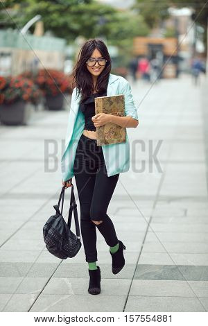 Asian student or school girl street portrait. Woman smiling and walking outside with backpack and book in casual business suite against blurred city space. Beautiful young mixed race Asian Caucasian woman.