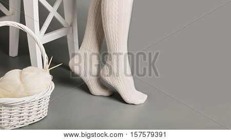 Female feet in white knitted tights near the basket with yarn and knitting.
