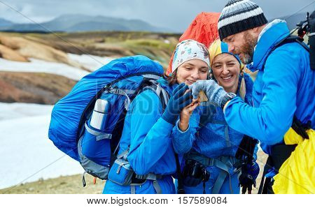 couple friends hikers un the Islandic mountains. two woman and one man photographer taking picture on the rhyolite mountains background in Iceland. people looking at the smartphone and laughs
