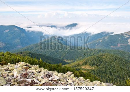 Beautiful landscape of the Carpathian mountains in autumn. Day. Stones against the hill covered with pine forest creeping pine and fluffy white clouds
