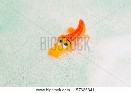 toy orange crocodile floating in the foamy water