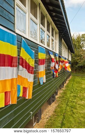 Buddhist Flag hung on a dark green wooden building. The Flag Was Designed In 19th Century To Symbolize And Universally Represent Buddhism And It Is Used By Buddhists Throughout The World