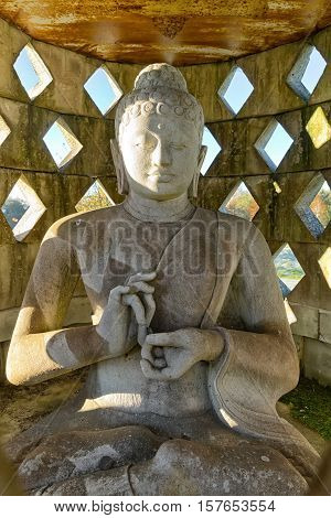Carved stone buddha statue inside small stupa. Frontal view