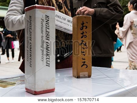 Tokyo, Japan - December 6, 2015: Omikuji is a fortune telling stick or paper. A tourist at the Meiji Shrine shakes a small box to receive their omikuji