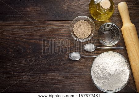 Baking wooden background with ingredients for pizza dough. Baking utensils on dark rustic table top view.
