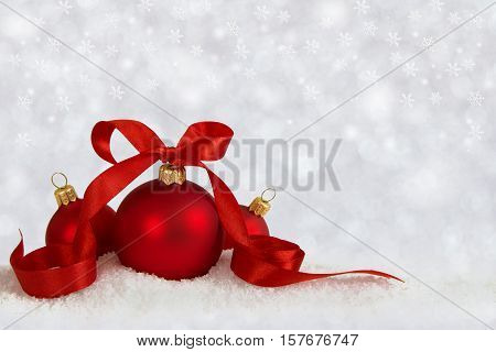 Three Christmas balls with red ribbon on artificial snow flakes. Defocused background with stars.