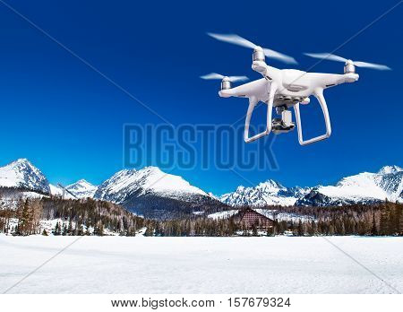 Hovering drone taking pictures of snowy white meadow and forest and clear blue sky