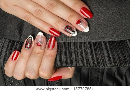 French manicure - beautiful manicured female hands with red black and white manicure with rhinestones  on black background