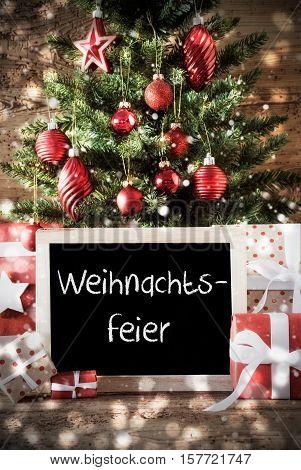 Chalkboard With German Text Weihnachtsfeier Means Christmas Party. Christmas Card For Seasons Greetings. Christmas Tree With Balls. Gifts Or Presents In The Front Of Wooden Background.