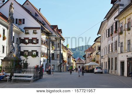 Gmina Škofja Loka, Škofja Loka Slovenia - September 25 2016: old town, Mestni trg (City Square). Typical buildings, windows decorated with flowers. Some people are on the street. On the left there is statue of Saint Mary.