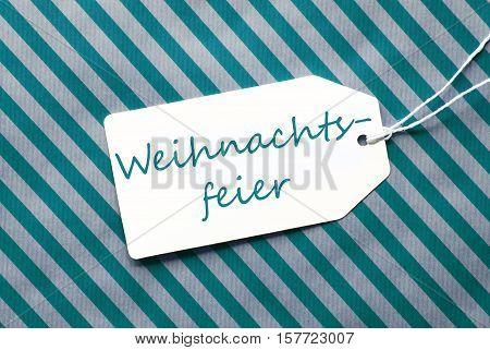 German Text Weihnachtsfeier Means Christmas Party. One Label On A Turquoise Striped Wrapping Paper. Textured Background. Tag With Ribbon.
